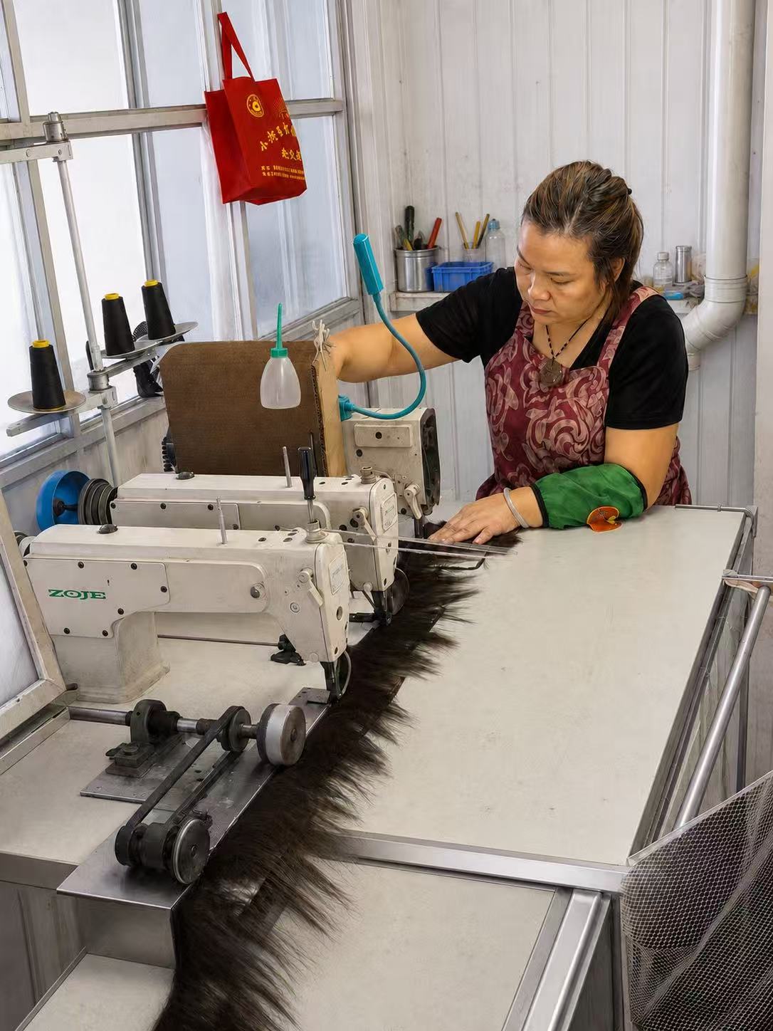 Production worker processing long human-hair bundles with an industrial machine.